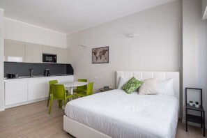 Une chambre d’hôtel moderne équipée d’un lit, d’un petit bureau, d’une chaise, d’un four à micro-ondes et d’une carte du monde accrochée au mur.