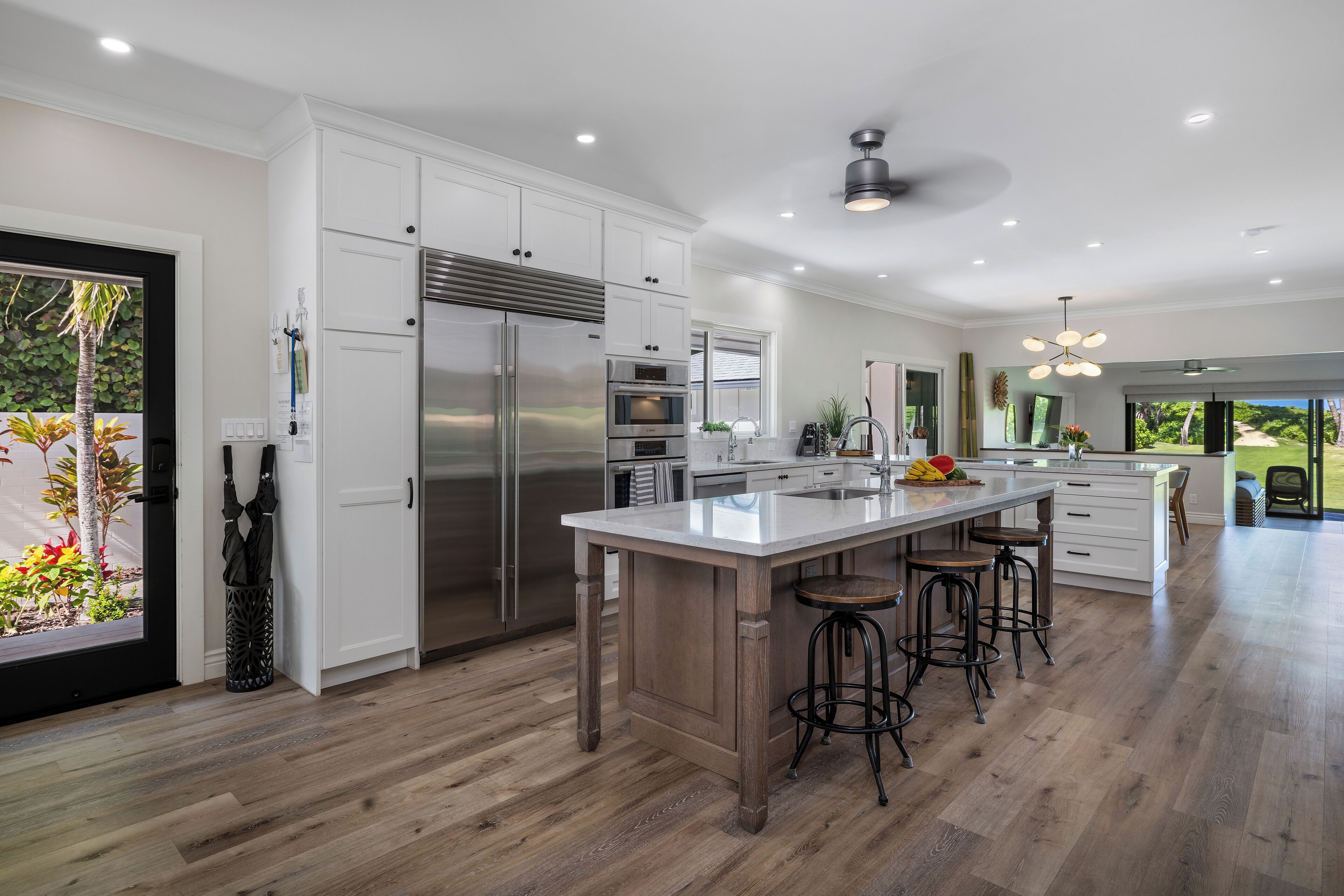 A modern kitchen with white cabinetry, stainless steel appliances, and a central island with stools.