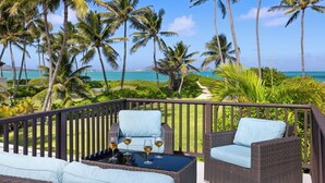 A balcony with wicker furniture and a glass table, overlooking a tropical beach with palm trees and a clear blue sky. - Hale Oahu Lic.#1990/NUC-1777/1778 BEACHFRONT KAILUA LUXURY (Kailua)
