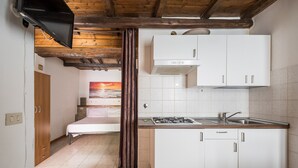 A compact kitchen with a stove, sink, and white cabinets. There's a bed with a view of the sunset in the background.