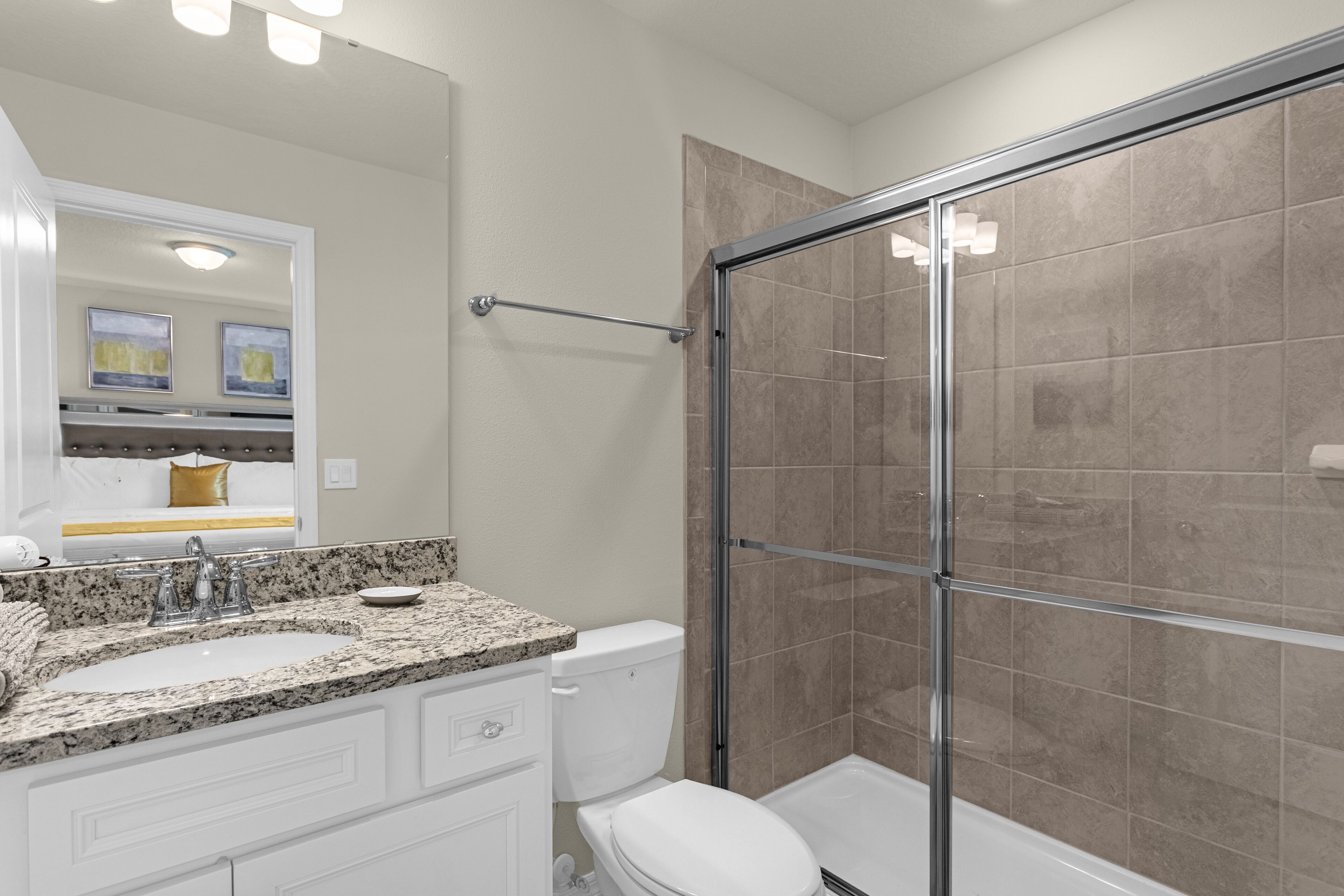 A bathroom with a granite countertop sink, a white toilet, and a glass shower enclosure.