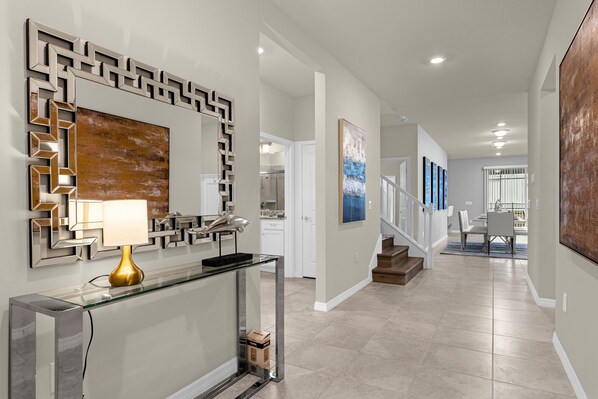 A modern hallway with a glass console table, a decorative mirror, and a staircase leading to a dining area. - Spectacular Resort Themed Luxury! LED Games Room - Prime Disney! (Davenport)