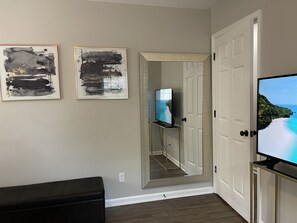 A room with a black leather sofa, a television on a stand, and two abstract paintings on the wall.