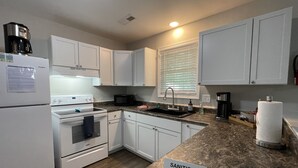 A kitchen with white cabinets, a stove, a microwave, a sink, and a countertop with a 'SANITIZED' sign. - King Suite Hot Tub Fireplace Fire Pit Foosball 1 (Ladson)