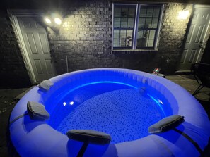 Un jacuzzi gonflable avec un éclairage bleu, entouré d’un mur de briques et agrémenté d’une fenêtre.