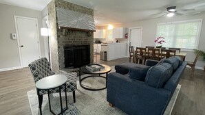 A living room with a fireplace, a sofa, a coffee table, and a dining area with chairs and a table. - King Suite Hot Tub Fireplace Fire Pit Foosball 1 (Ladson)