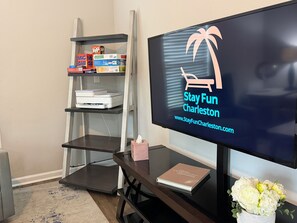 Habitación con una televisión que muestra 'Stay Fun Charleston' y una estantería con diversos objetos.