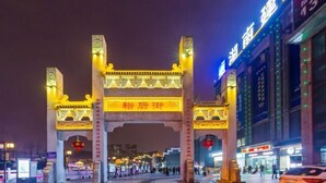 Une arche illuminée de mille feux, ornée de caractères chinois traditionnels, entourée de bâtiments modernes et bordée par une rue animée la nuit.
