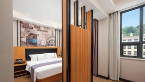 Une chambre d’hôtel avec un lit, un séparateur en panneaux de bois, une grande fenêtre avec des rideaux et un mur orné d’une image d’un tramway d’époque.