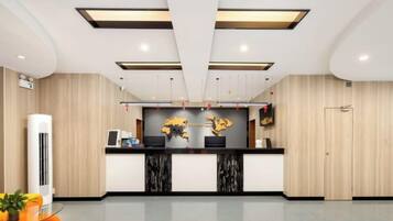 A reception area with a reception desk, two black marble counters, a wall-mounted display, and a potted plant.
