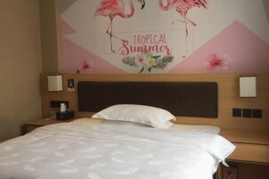 Habitación de hotel con cama, cabecera, dos mesitas de noche y un mural con flamencos y el texto 
