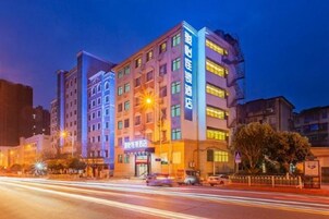 A multi-story hotel with illuminated signage, a visible entrance, and a street view with passing vehicles.