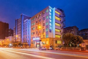 Een meerlaags hotel met verlichte signage, een vluchttrap en een straatbeeld met bewegende voertuigen.