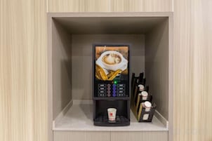 Una cafetera con portacopas y una pequeña figura decorativa en un estante.