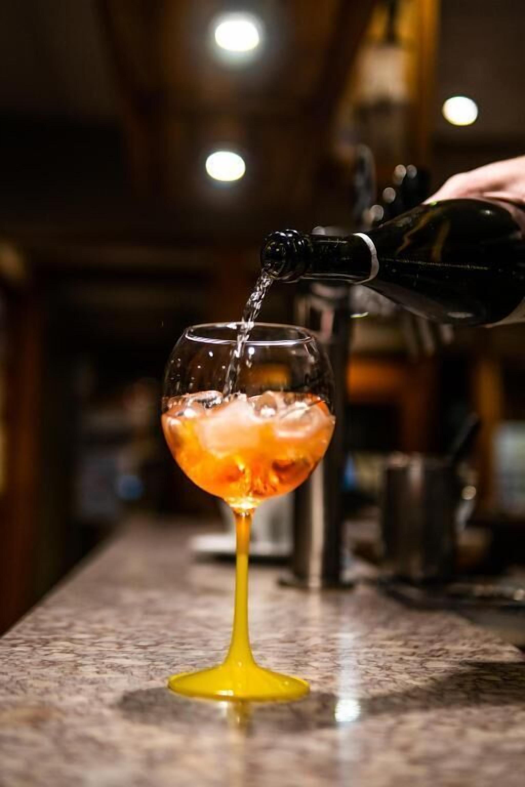 A cocktail being poured into a glass with a yellow stem.