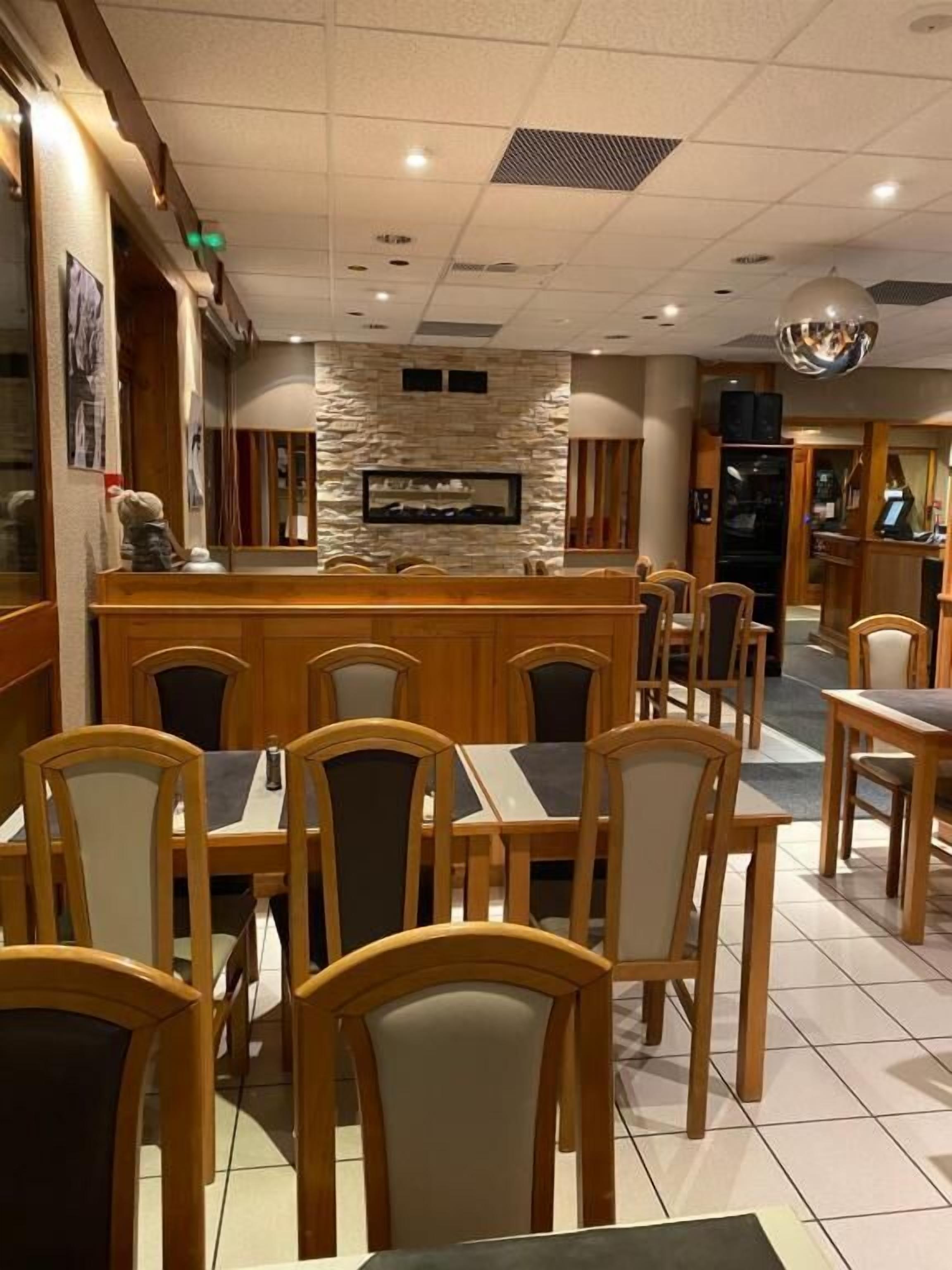 A restaurant with wooden tables and chairs, a stone wall, and a bar area.