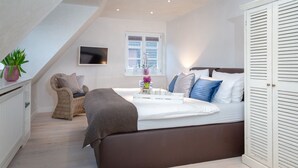 A bedroom with a bed, a chair, a TV, a window, and a wardrobe. - large modern beach house style apartment (Sylt)