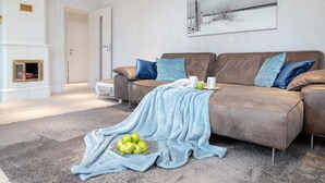 A modern living room with a brown leather sofa, a blue throw blanket, and a bowl of green apples on a grey rug. - large modern beach house style apartment (Sylt)