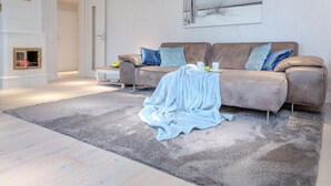 A modern living room with a beige sofa, blue cushions, a grey rug, and a fireplace. - large modern beach house style apartment (Sylt)
