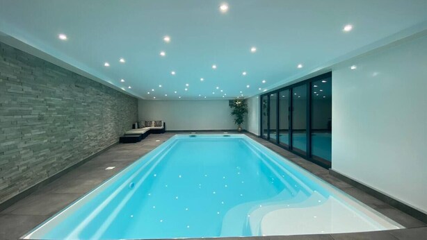 Ein großer Innenpool mit einer Steinwand und einer Bank, umgeben von einer Glaseinfassung.