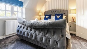 Ein Schlafzimmer mit einer gesteppten Kopfteil, einem großen Fenster mit blauen Vorhängen und einem Heizkörper.
