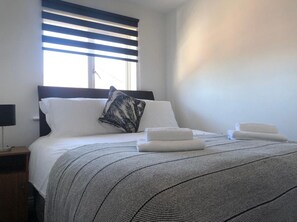 Relax in comfort with a large bed, striped blanket, and a nightstand with a lamp.