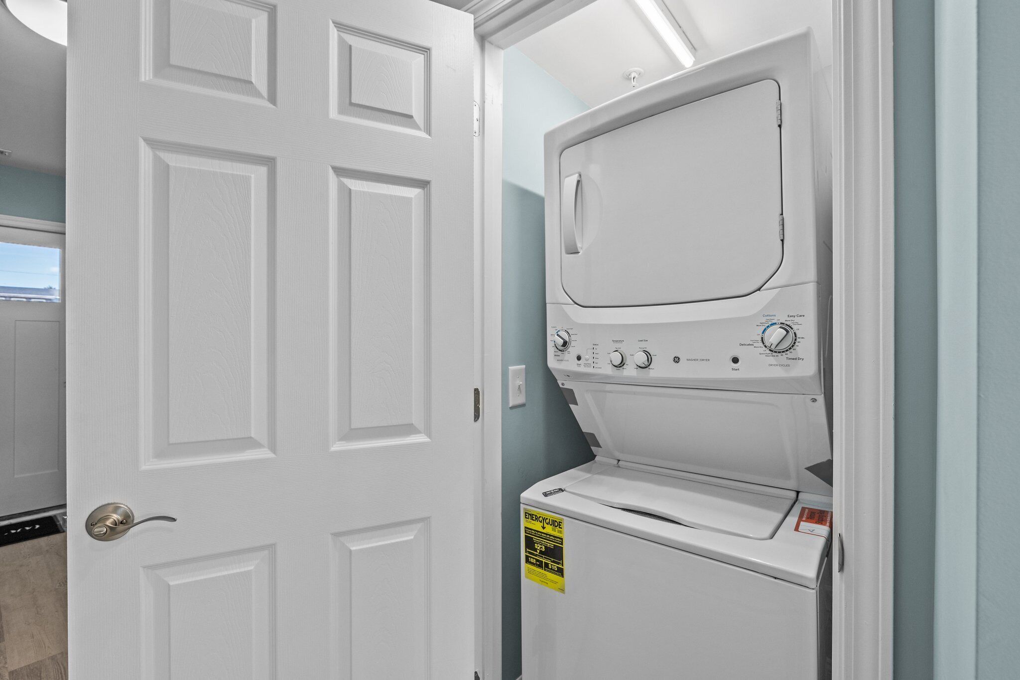 A laundry room with a front-loading washer and dryer, a door with a doorknob, and a light switch on the wall.
