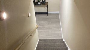 Una scala rivestita di moquette con un corrimano, un tavolino con una pianta e un lampadario a parete.