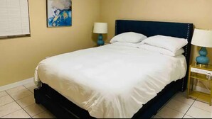 Un letto rifatto con cura in una stanza dalle pareti color beige, un quadro e un comodino con una lampada.