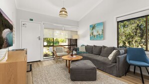 A modern living room with a grey sofa, a blue chair, a wooden coffee table, and a large window with a view of greenery. - Orion Retreat by Experience Jervis Bay (Vincentia)