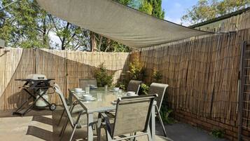 An outdoor patio with a table and chairs, a grill, and a bamboo fence.