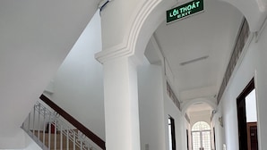 En gang med hvide vægge, en trappe med hvide gelændere og et hvælvet loft. Et grønt skilt over læser "LOI THOAT EXIT".