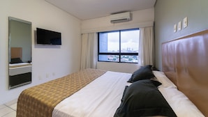 A hotel room with a bed, a TV mounted on the wall, an air conditioning unit, and a window with a city view. - Flat na Ilha do Leite, Recife 1 quarto. Conforto e Excelente localização OTH1603 (Recife)