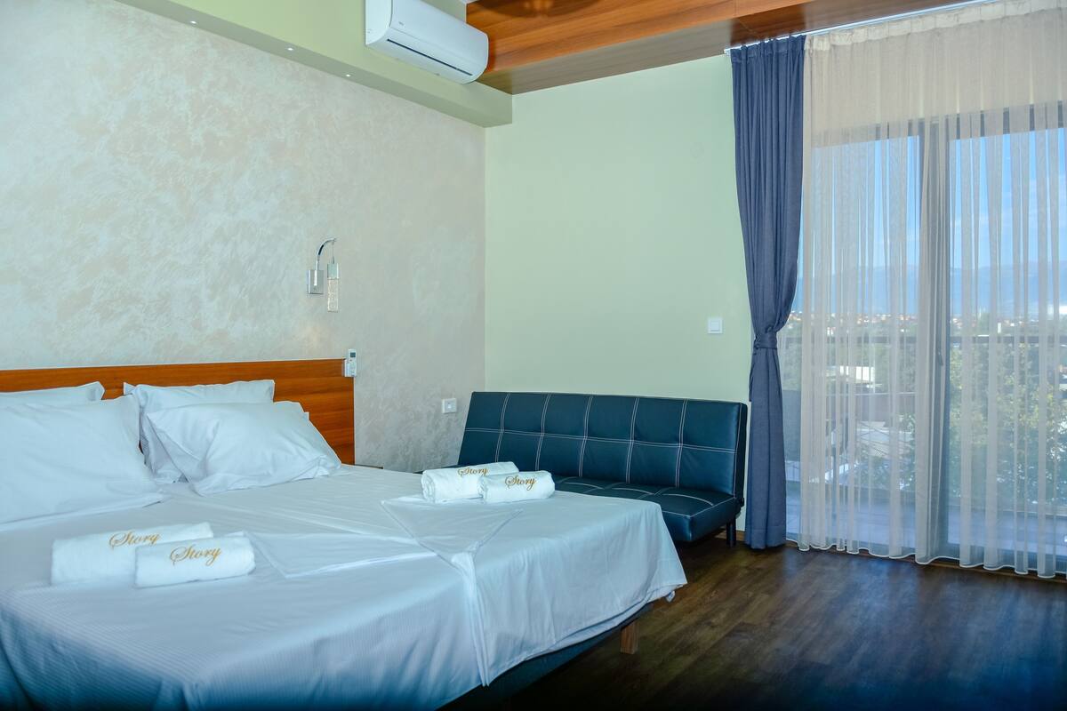 Habitació d'hotel amb llit, sofà i una finestra gran amb cortines.