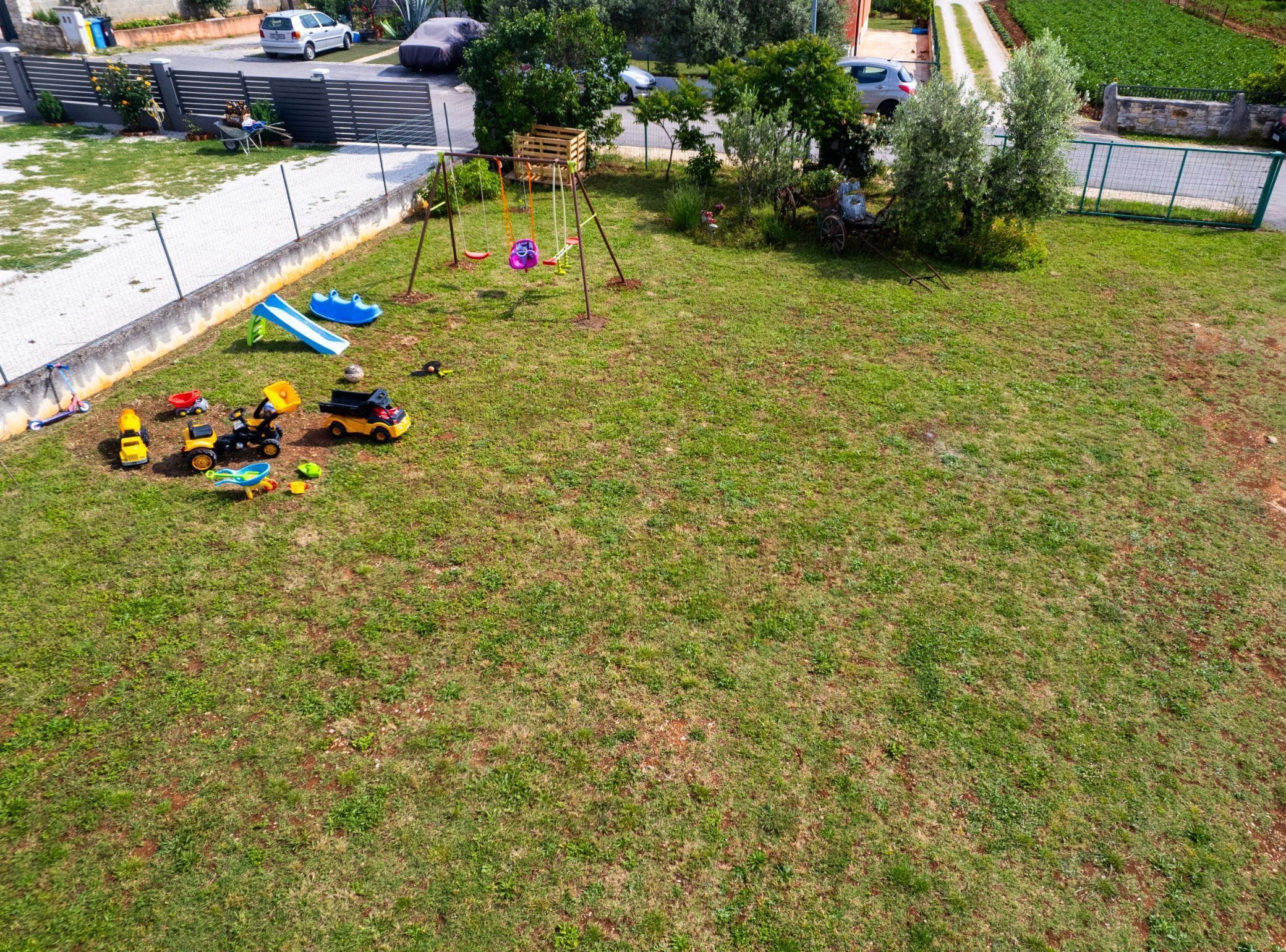 A grassy outdoor area with a swing set, a small pond, and toy vehicles.