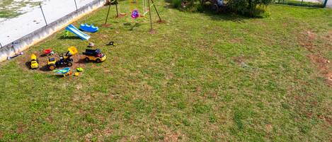A grassy outdoor area with a swing set, a small pond, and toy vehicles.