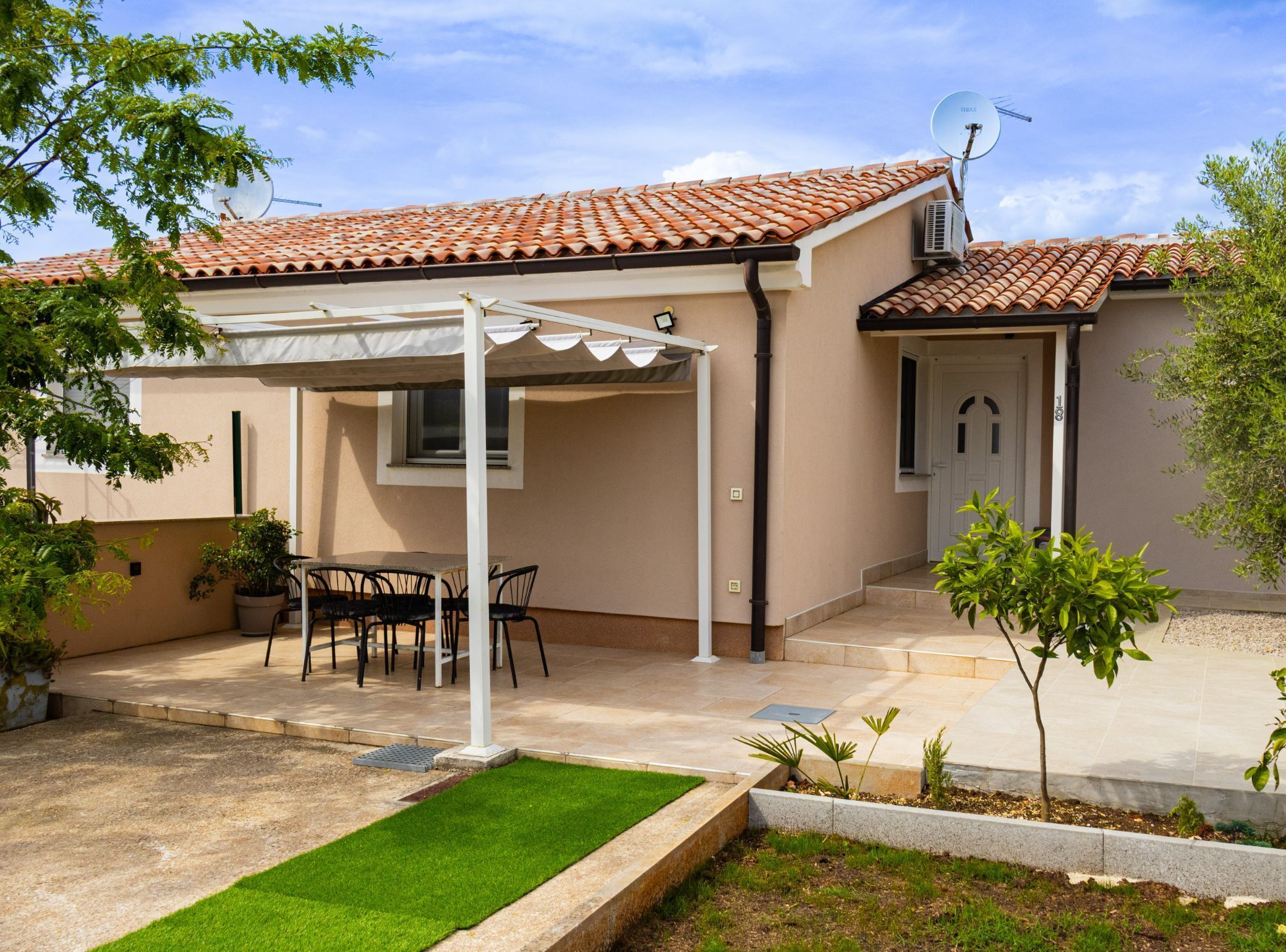 A house with a tiled roof, a covered patio with a table and chairs, and a small garden area.