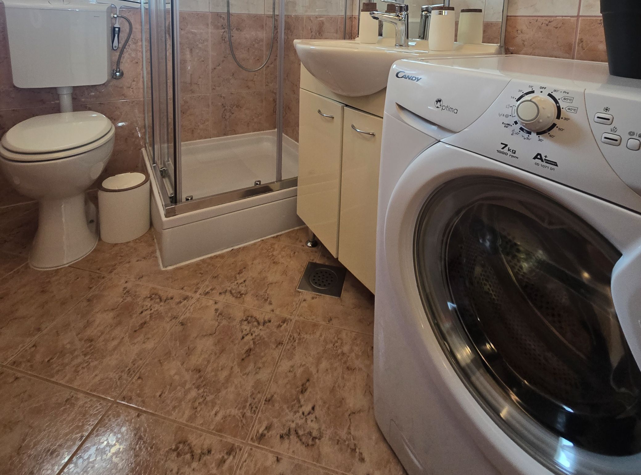 A bathroom with a toilet, shower, and washing machine.