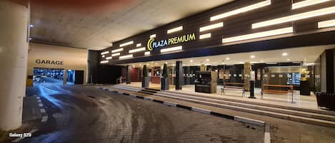 En modern byggnad med en skylt som visar att det är en "Plaza Premium"-anläggning, en entré märkt "Garage" och ett område som är inrett som en "matmarknad".