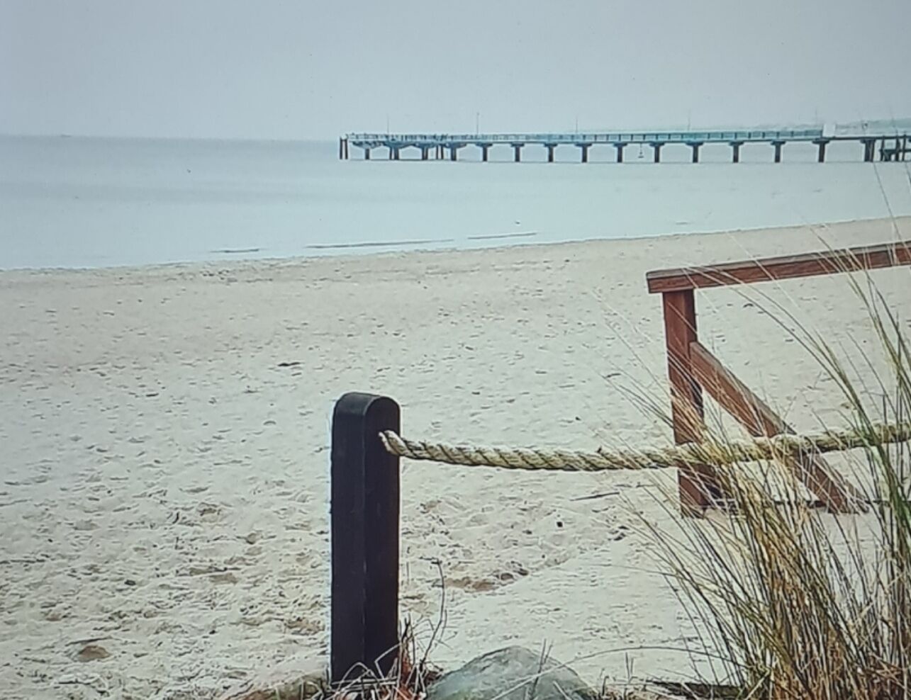 Una playa con un banco de madera y una barrera de cuerda.