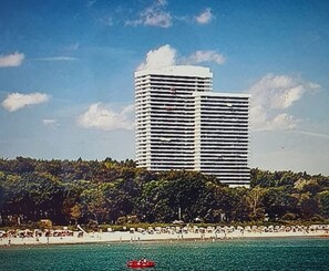 Un hotel alto y moderno con techo plano y líneas horizontales, cerca de una playa bajo un cielo azul despejado.