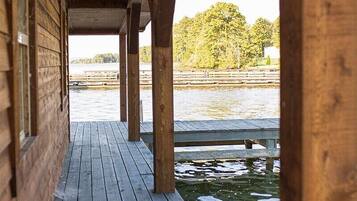 A wooden pier extending over water, supported by wooden beams, with a view of trees and a distant shoreline.