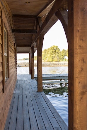 A wooden pier extending over water, supported by wooden beams, with a view of trees and a distant shoreline.