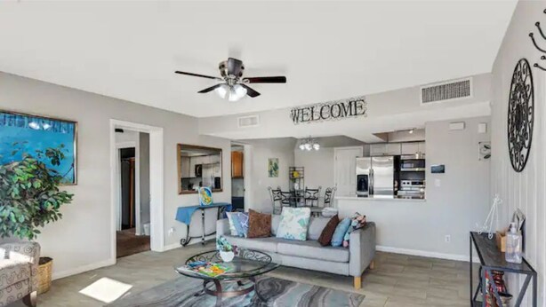 A spacious living room with a gray sofa, a coffee table, and a ceiling fan. A 'WELCOME' sign is visible on the wall. - Historic Scottsdale Home with Modern design (Scottsdale)