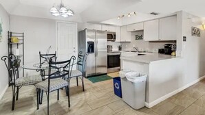 A modern kitchen with white cabinetry, a stainless steel refrigerator, a microwave, and a sink. There is a dining area with a glass table and metal chairs. - Historic Scottsdale Home with Modern design (Scottsdale)