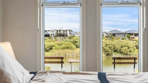 Ein Schlafzimmer mit großem Fenster und Blick auf eine angelegte Grünfläche mit Teich und Gebäuden.