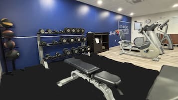 Un gimnasio con bancos, mancuernas y equipo cardiovascular.