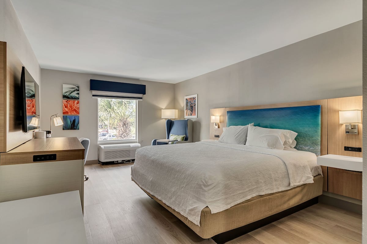 Una habitación de hotel moderna con una cama grande, un escritorio, una silla, un televisor y obras de arte en las paredes.
