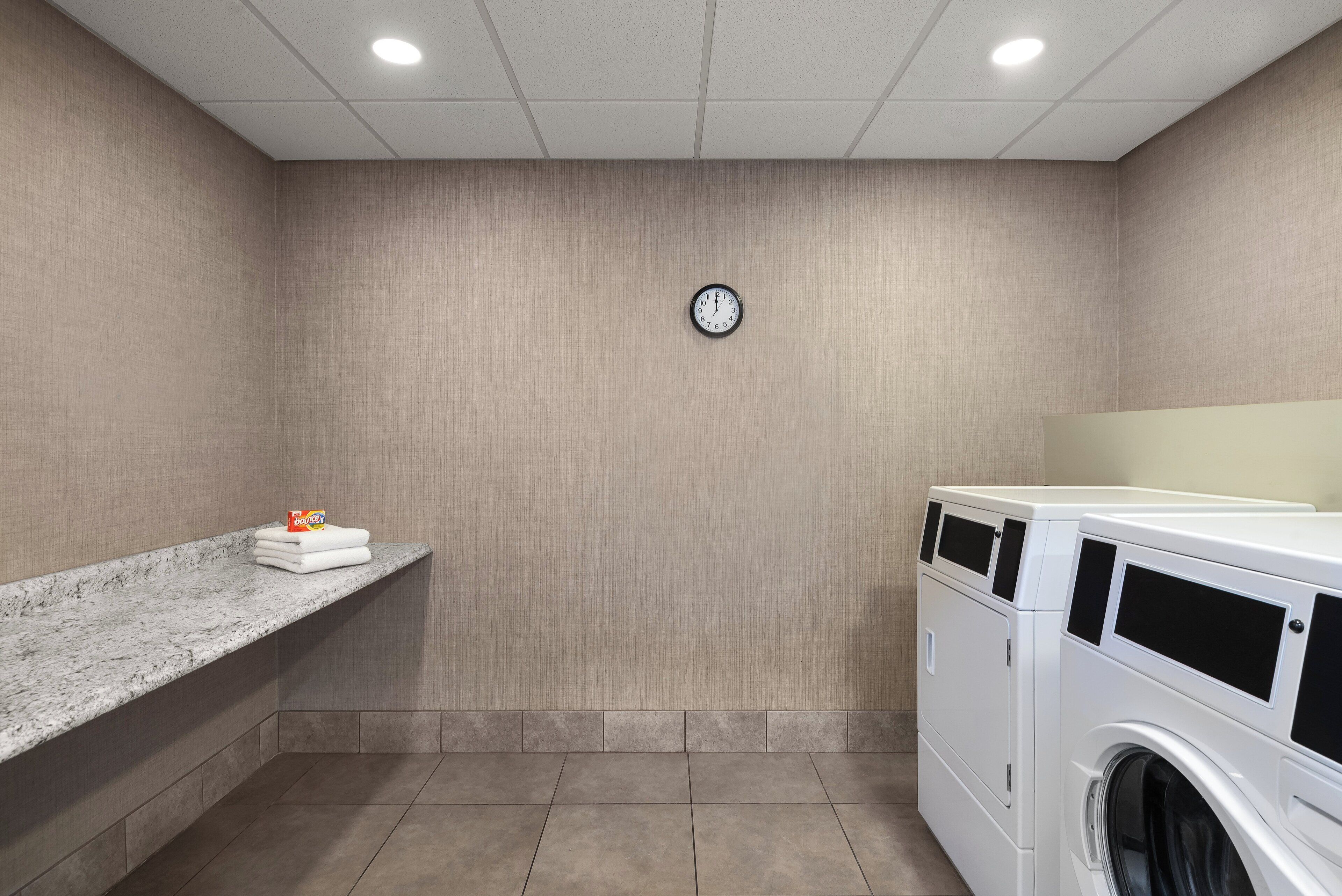 A laundry room with a clock on the wall, a marble countertop with towels, and stacked laundry baskets.