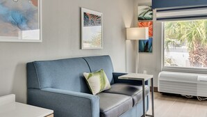 Una sala moderna con un sofá azul, una mesita y una ventana con vista a palmeras.